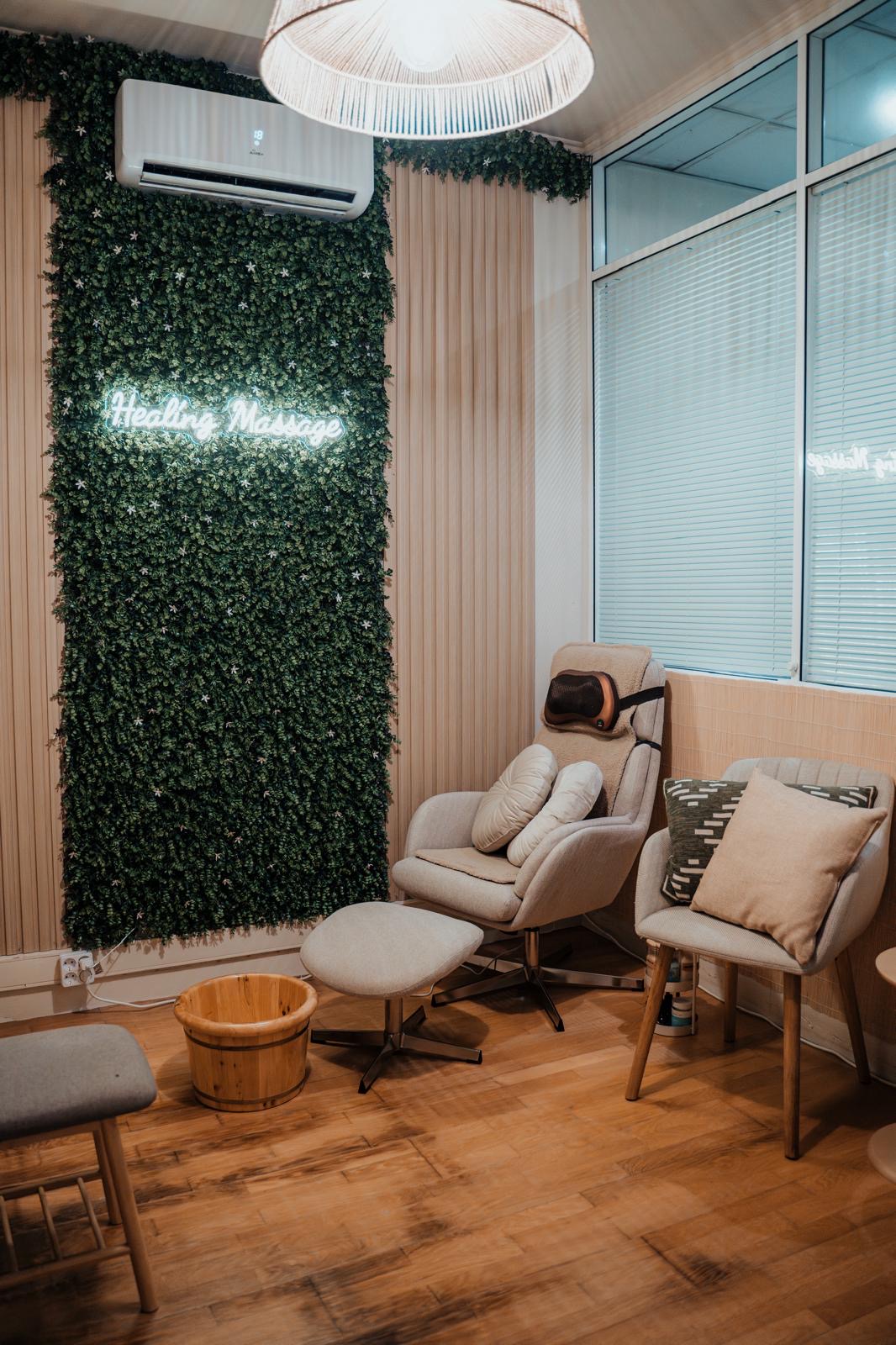 Espaço Healing Massage com parede verde, letreiro luminoso e poltrona de massagem
